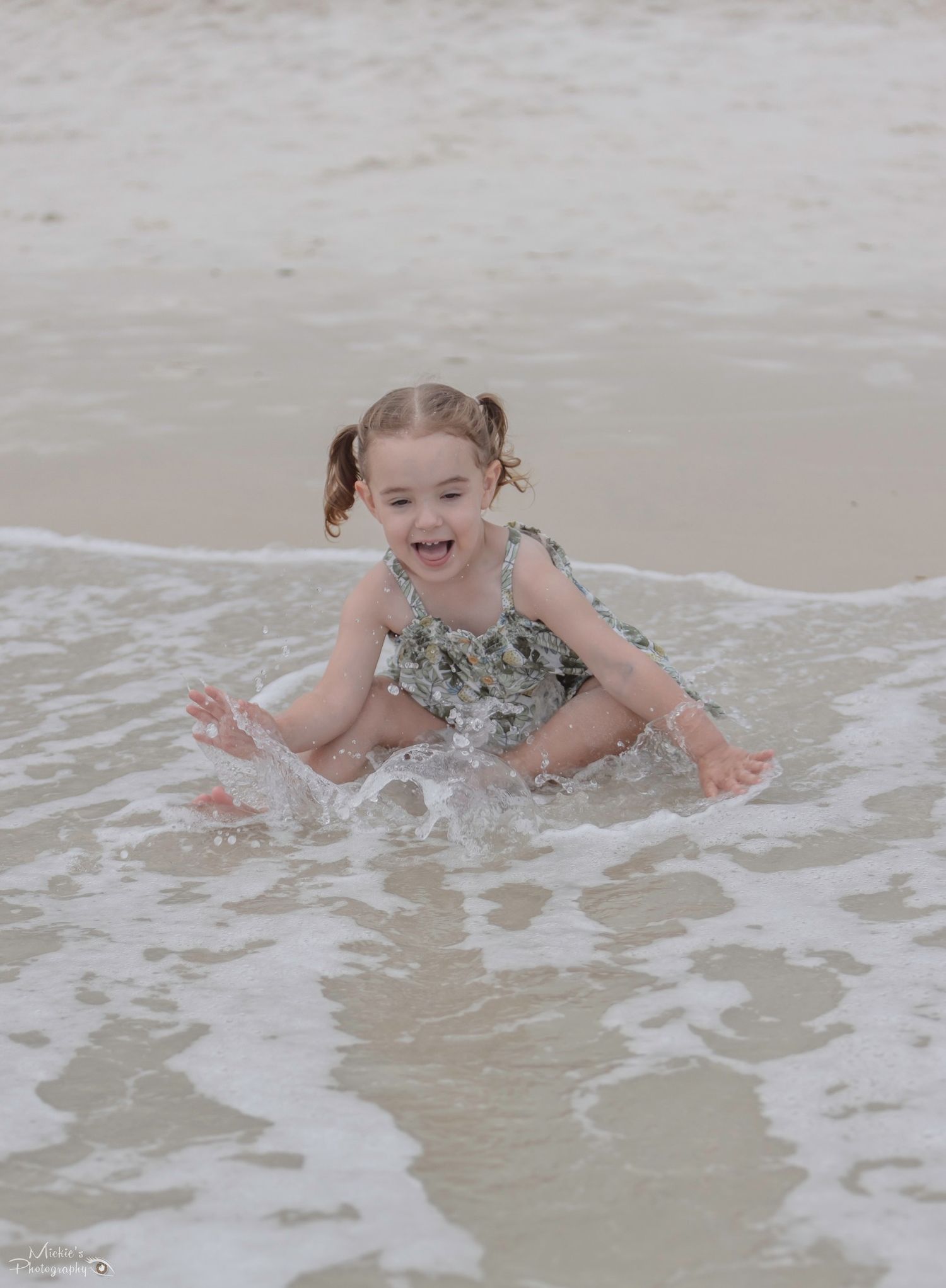 Child splashing and playing in ocean waves at beach.