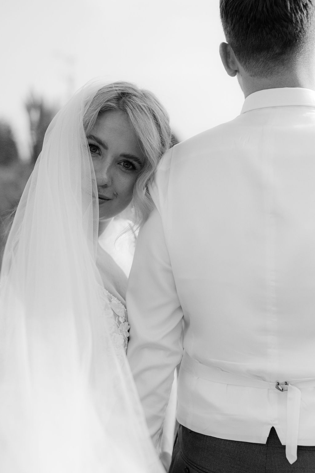 Artistic black and white portrait showing bride in veil next to groom.