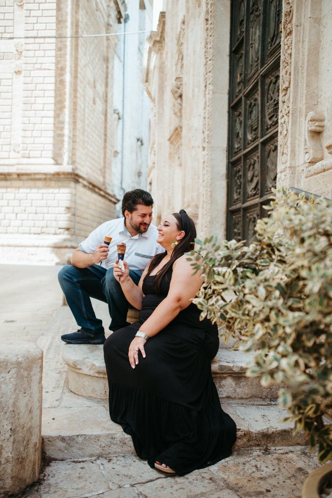 Playful couple posing against white stone building wall.