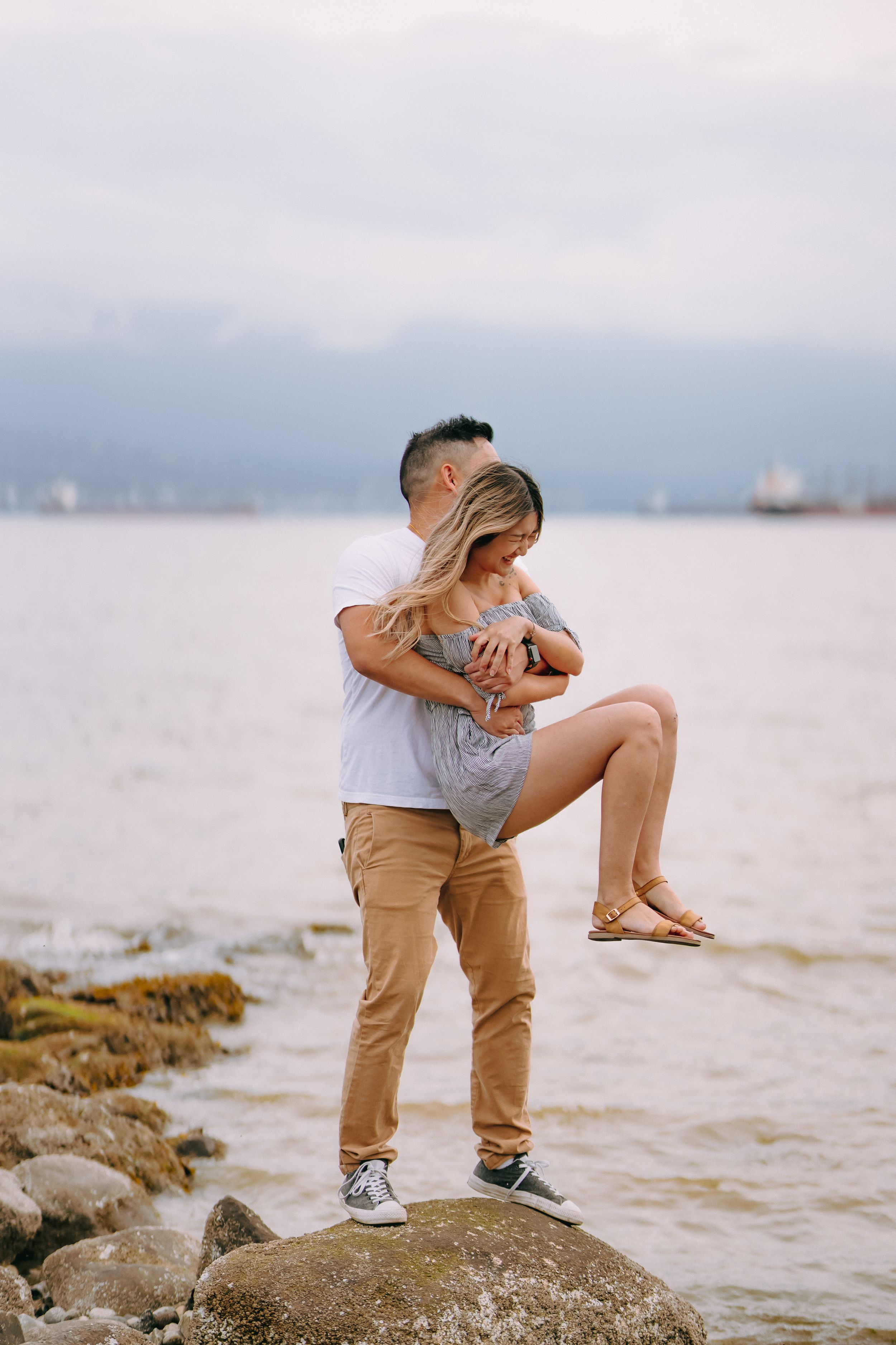 Two people share an intimate moment sitting on rocks by the ocean at sunset.