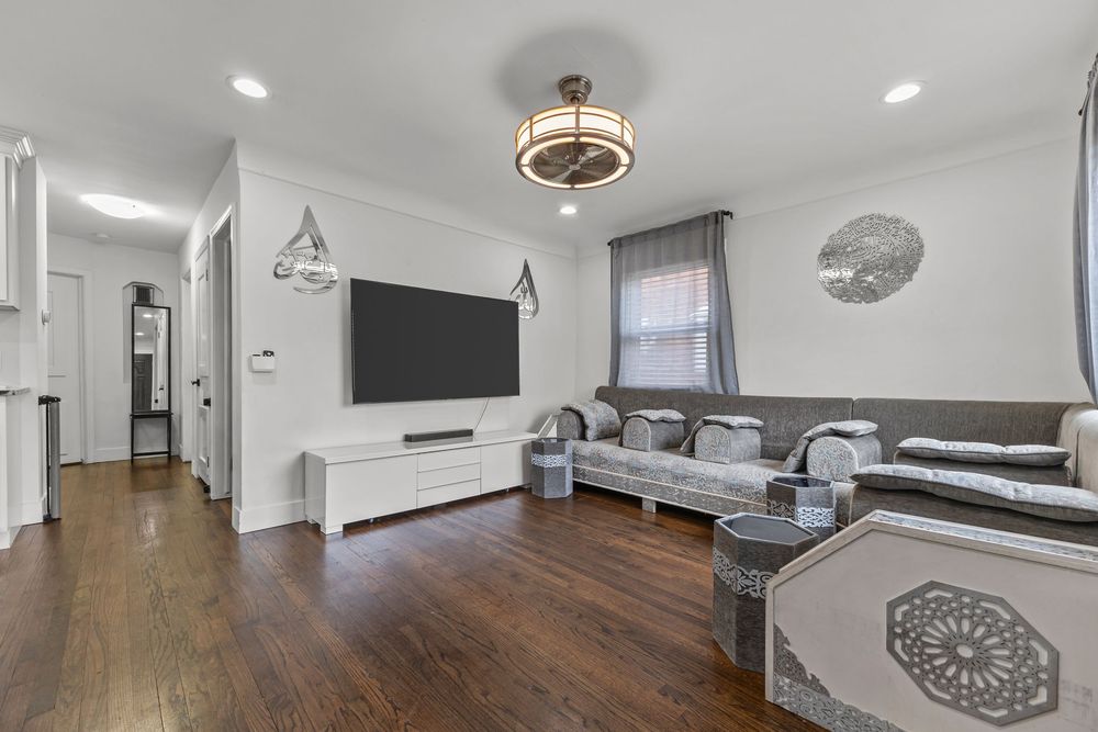 Spacious living room with dark hardwood floors, recessed lighting, and large wall-mounted TV.