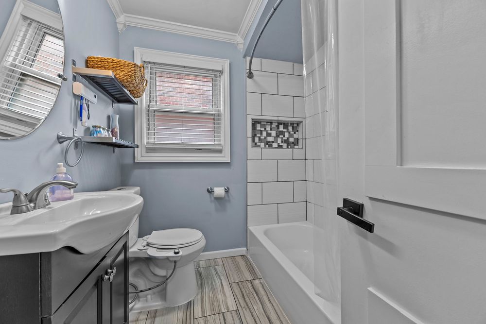 Clean bathroom with blue walls, white subway tile shower, dark vanity, crown molding, and wood-look vinyl floors.