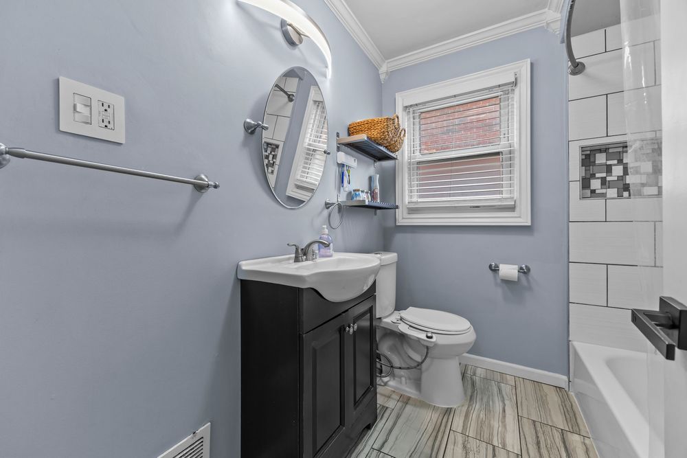 Updated bathroom with blue walls, dark vanity, oval mirror, white subway tile tub surround, and wood-look floors.