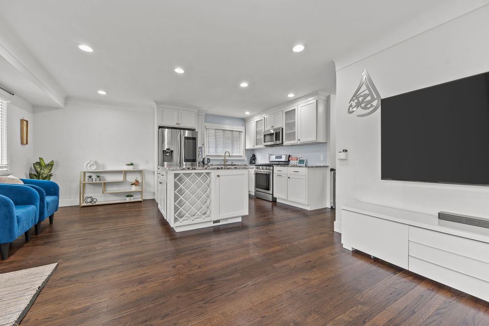 Open concept kitchen and living room with white cabinets, kitchen island, dark hardwood floors, and large TV.