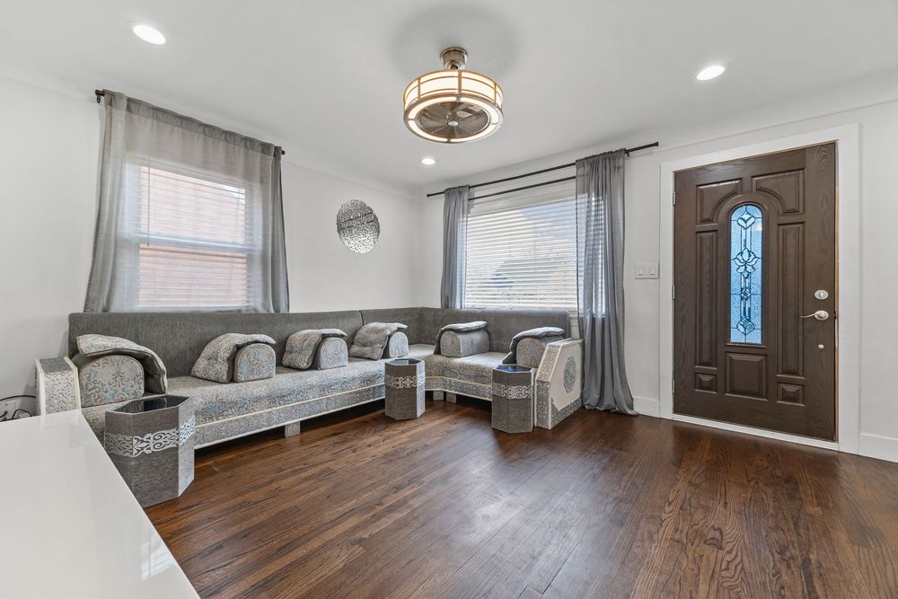 Bright living room with dark hardwood floors, gray sofas, decorative front door, and chandelier.