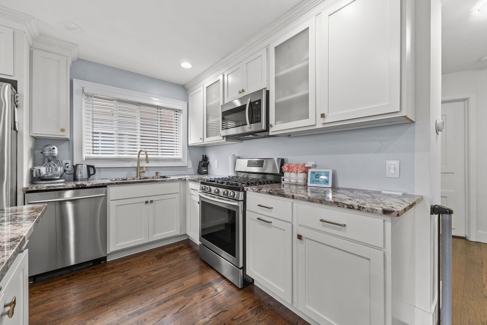 White kitchen with stainless steel appliances, granite countertops, glass cabinets, and hardwood floors.
