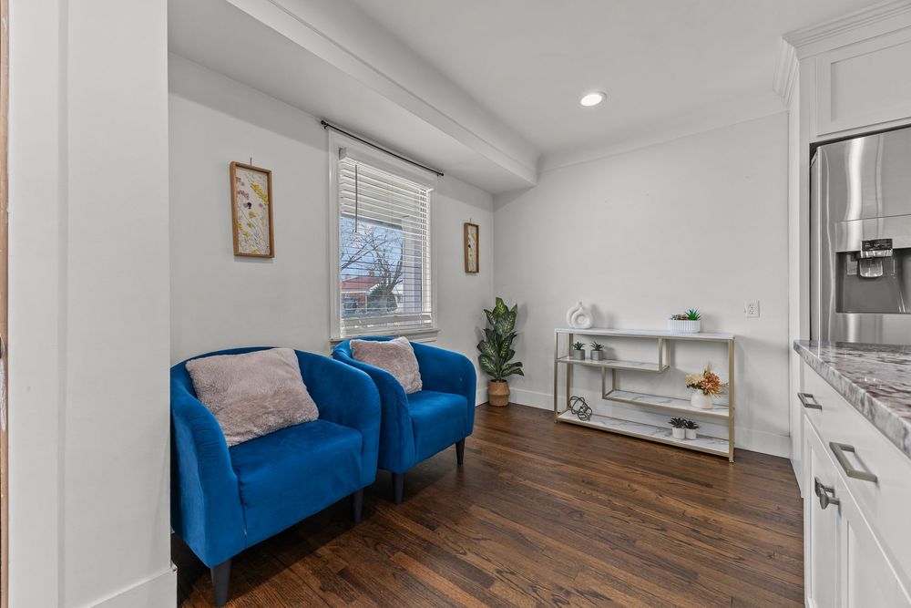 Cozy sitting area with two blue velvet accent chairs, dark hardwood floors, and bright window in modern home.
