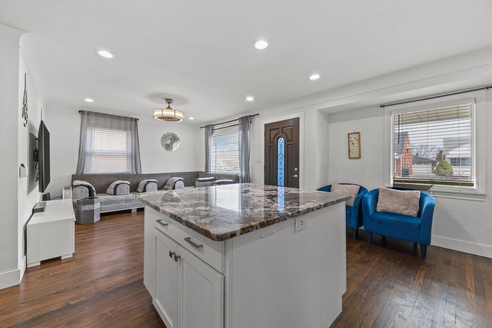 Spacious open floor plan featuring white kitchen island with granite top, hardwood floors, and blue accent chair.