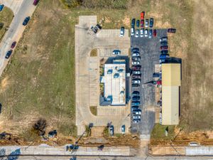 Bird's eye view of a small commercial property with parking lot and vehicles arranged in neat rows.