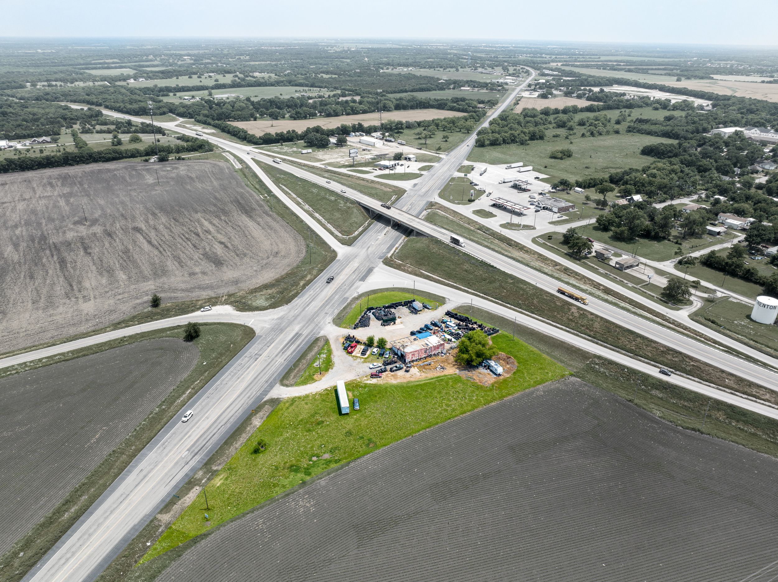 Aerial view of highway intersection with commercial buildings and farmland in rural area.