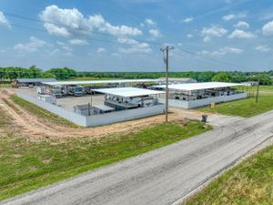 Aerial view of storage units and covered parking facilities surrounded by rural landscape under blue sky.