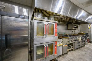 Professional restaurant kitchen featuring commercial ovens, stainless steel appliances and exhaust hoods.