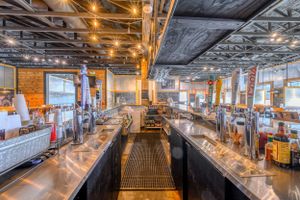Modern industrial bar interior with exposed ceiling and long counters equipped with multiple beer taps.