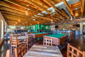 Rustic game room with wooden beams, pool table, and casual dining furniture in an open layout.
