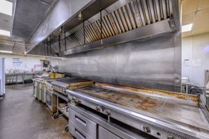 Commercial kitchen with stainless steel cooking equipment and ventilation hood system.