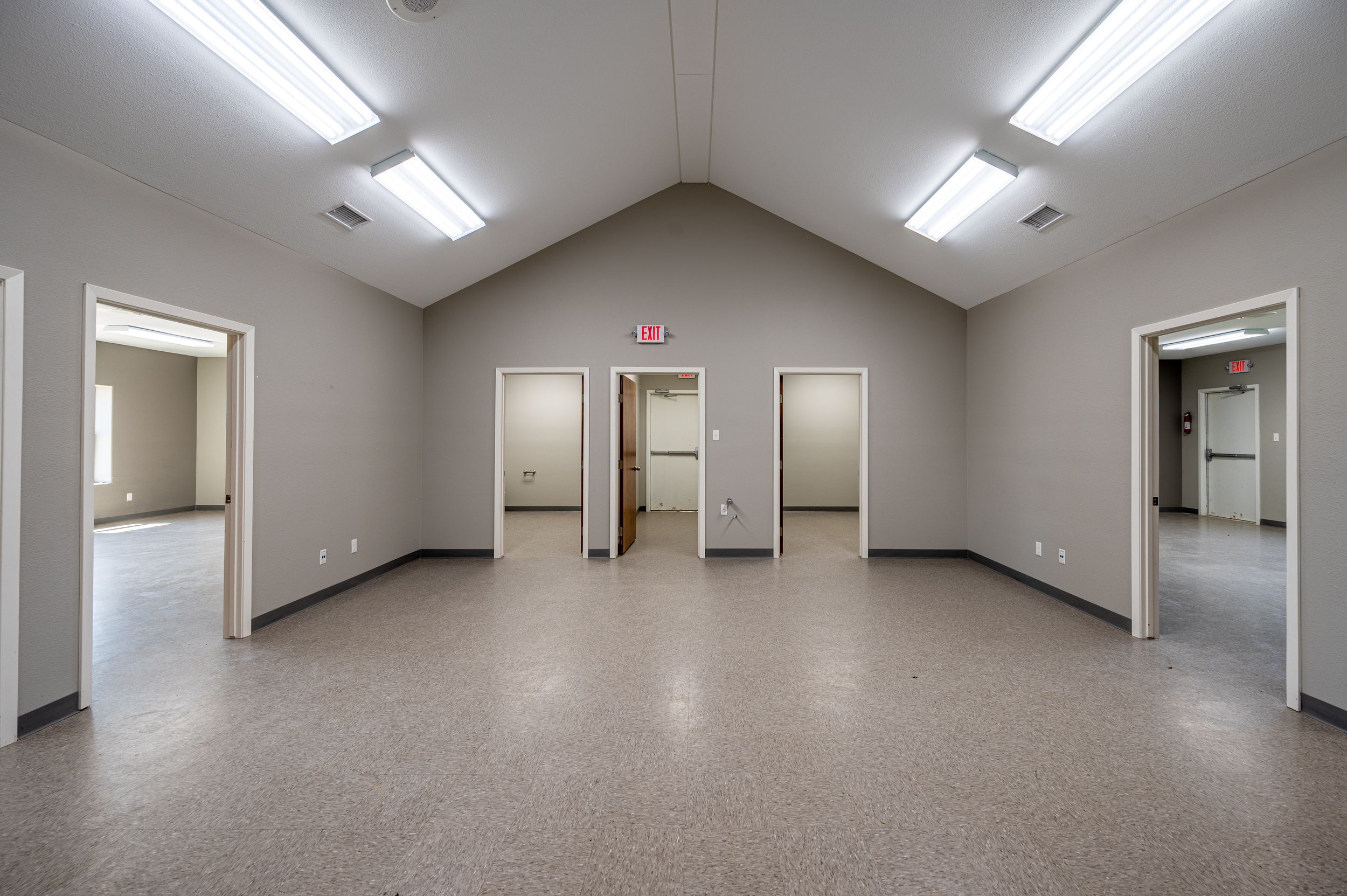 Empty commercial office space with vaulted ceiling, fluorescent lighting, and multiple doorways.