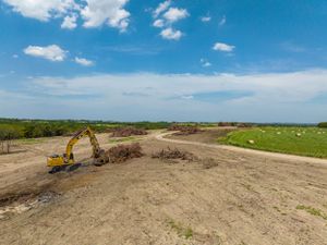 Construction site with yellow excavator working on dirt road under blue sky with white clouds.