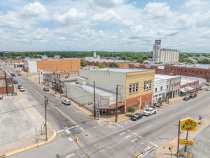 Historic downtown street view showing brick buildings, storefronts and parked cars along a wide thoroughfare.