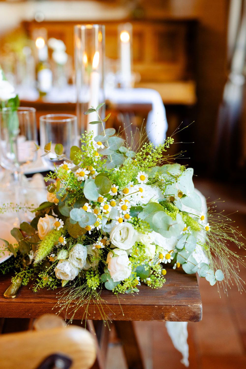 Lush white and green floral centerpiece with mixed flowers and foliage on wooden dining table.