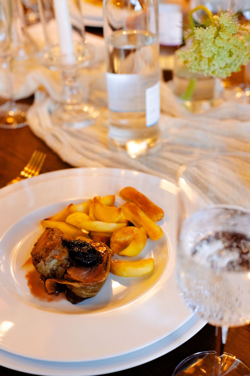 Plated dish with roasted meat and yellow potatoes served on elegant table setting.