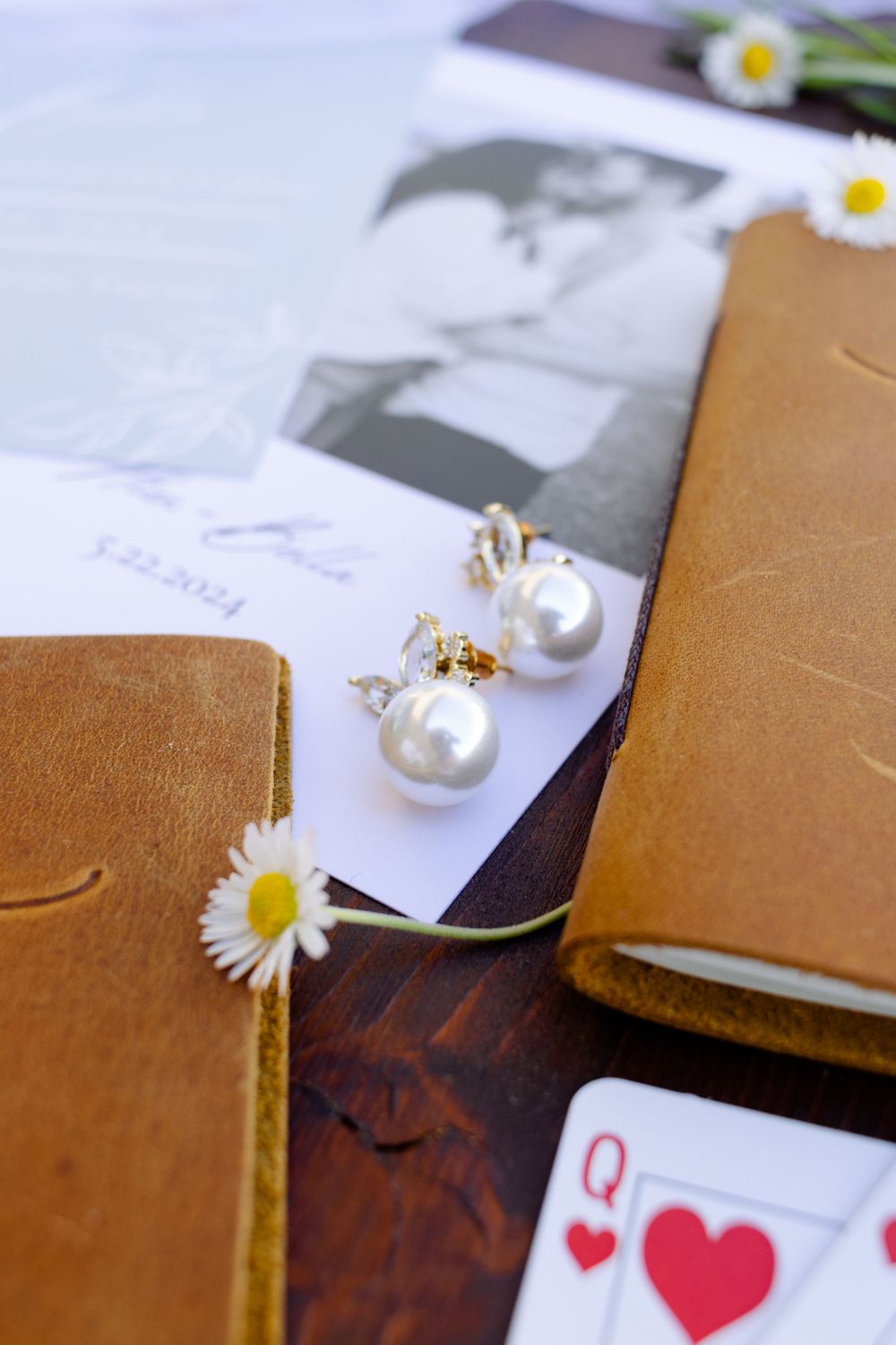 Wedding details with pearl jewelry and playing cards on brown leather surface.