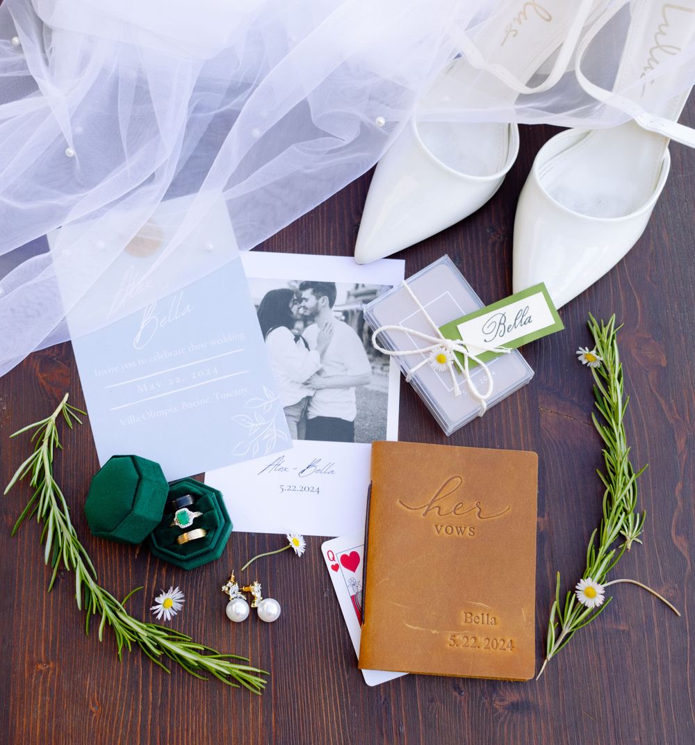 Wedding accessories including white tulle, jewelry, and green velvet ring boxes arranged on a dark wooden surface.