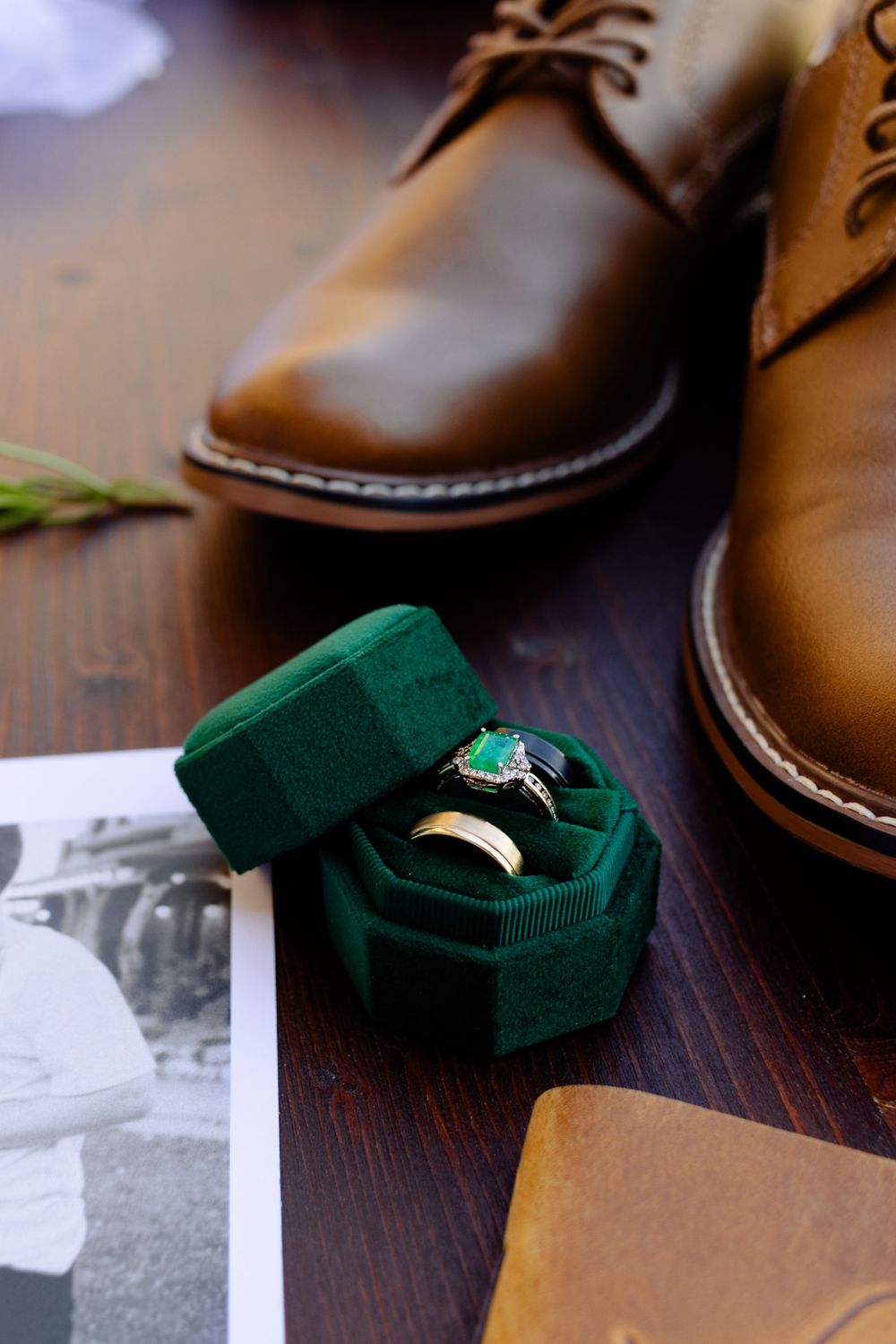 Brown leather dress shoes and green velvet ring box on wooden surface with black and white photo.