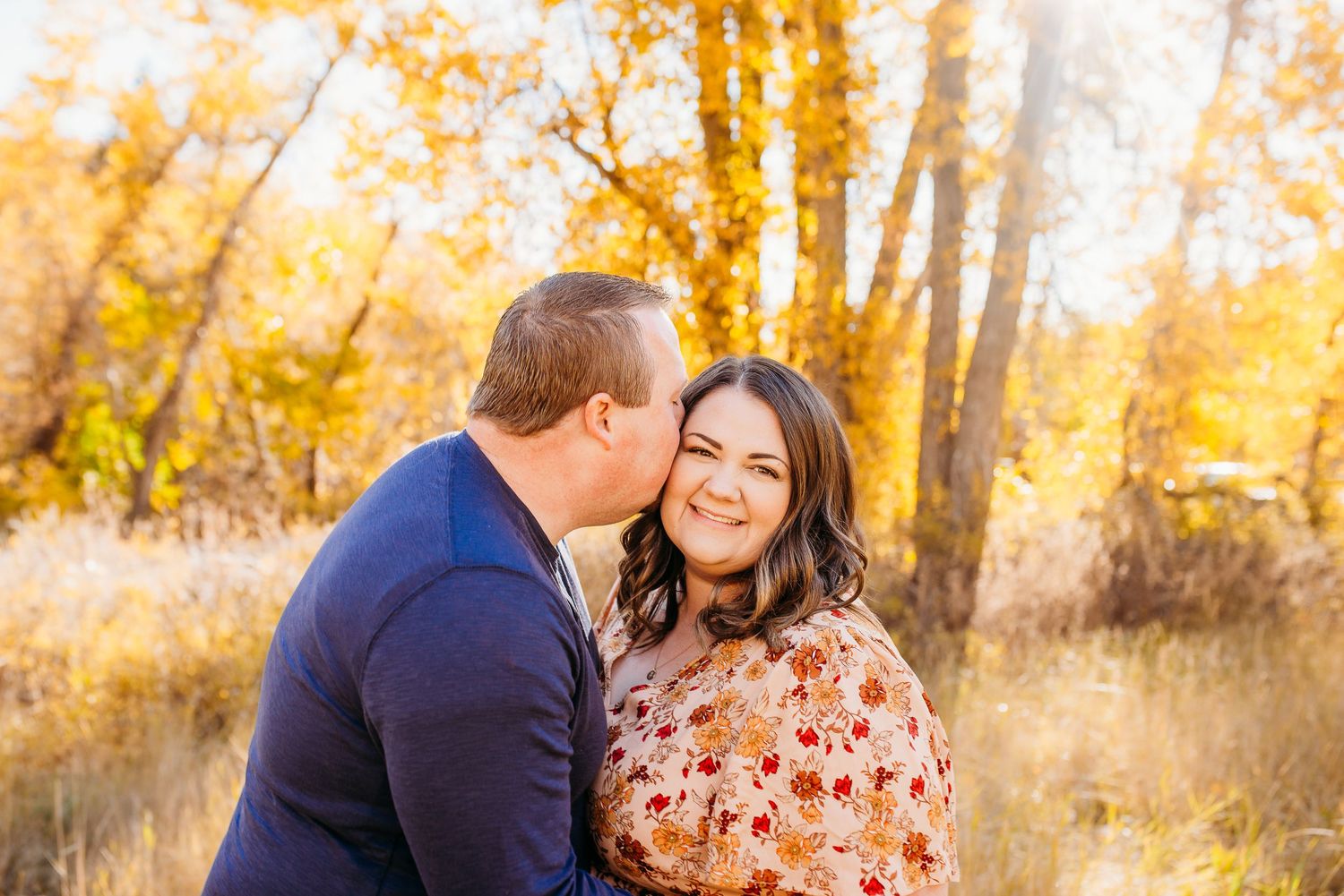 Couple sharing intimate moment together in field with golden autumn foliage behind them.