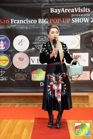 A presenter in a black dress with tiger design speaks on stage at the Bay Area Visits pop-up show.
