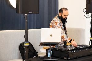 A DJ performs with a laptop and mixing equipment at an indoor event.