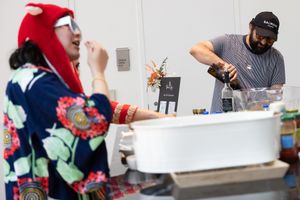 Two people prepare beverages at a white bar station during an indoor event.