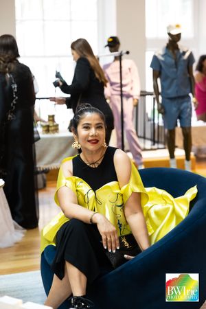 A guest in a black and yellow outfit sits on a blue couch during an indoor event.