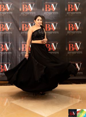A flowing black evening gown twirls against a step-and-repeat backdrop at an event.