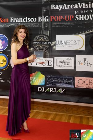 A purple evening gown is showcased at the San Francisco Big Pop-Up Show with sponsor logos.