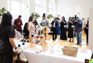 Vendors and attendees mingle at a pop-up market event with display tables in a bright sunlit room.