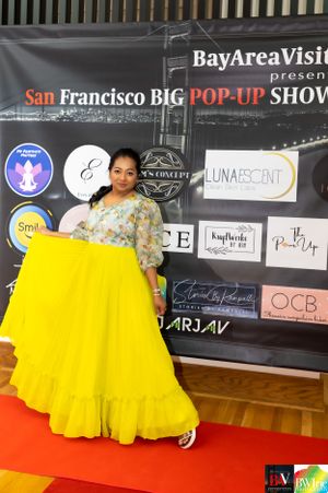 Model in bright yellow floor-length gown poses at San Francisco BIG Pop-Up Show banner wall.