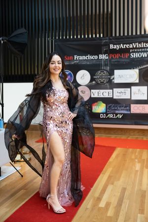 Model strikes pose in sequined gown with high slit and sheer black overlay at fashion show.