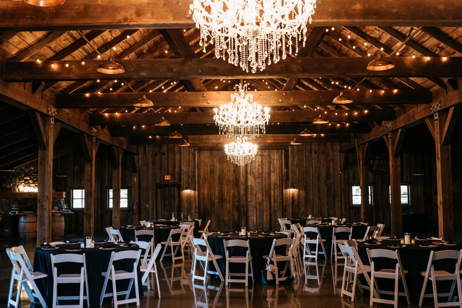 Elegant barn wedding reception venue with crystal chandeliers and white folding chairs.