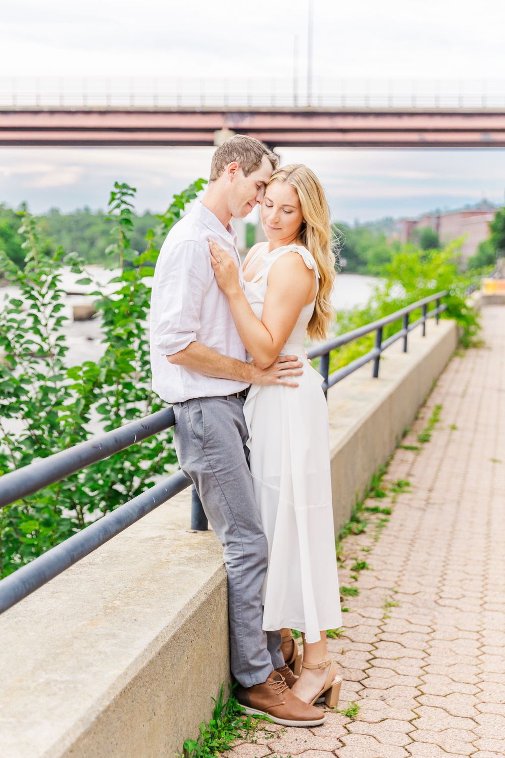 A couple in white and gray outfits share an intimate moment by a railing.
