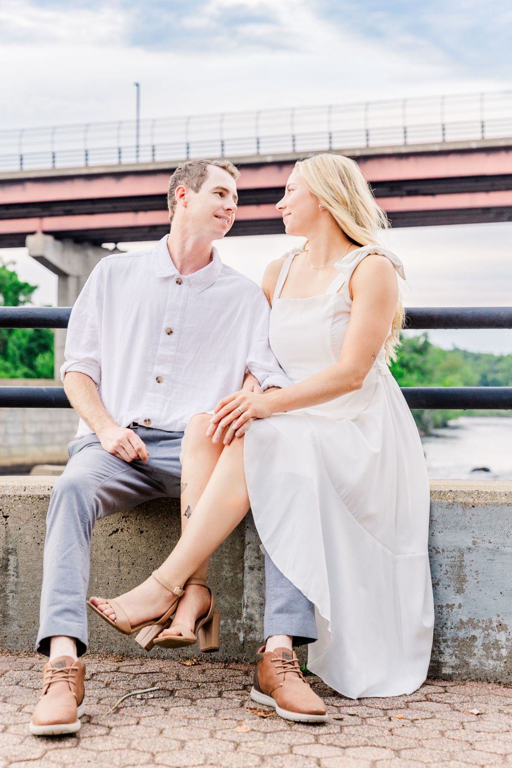 Couple sitting together on concrete wall enjoying intimate moment near bridge.