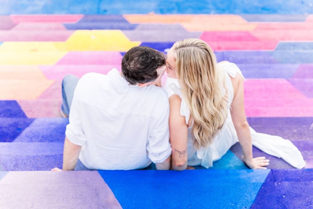 Couple resting on vibrant rainbow painted stairs during intimate photoshoot.