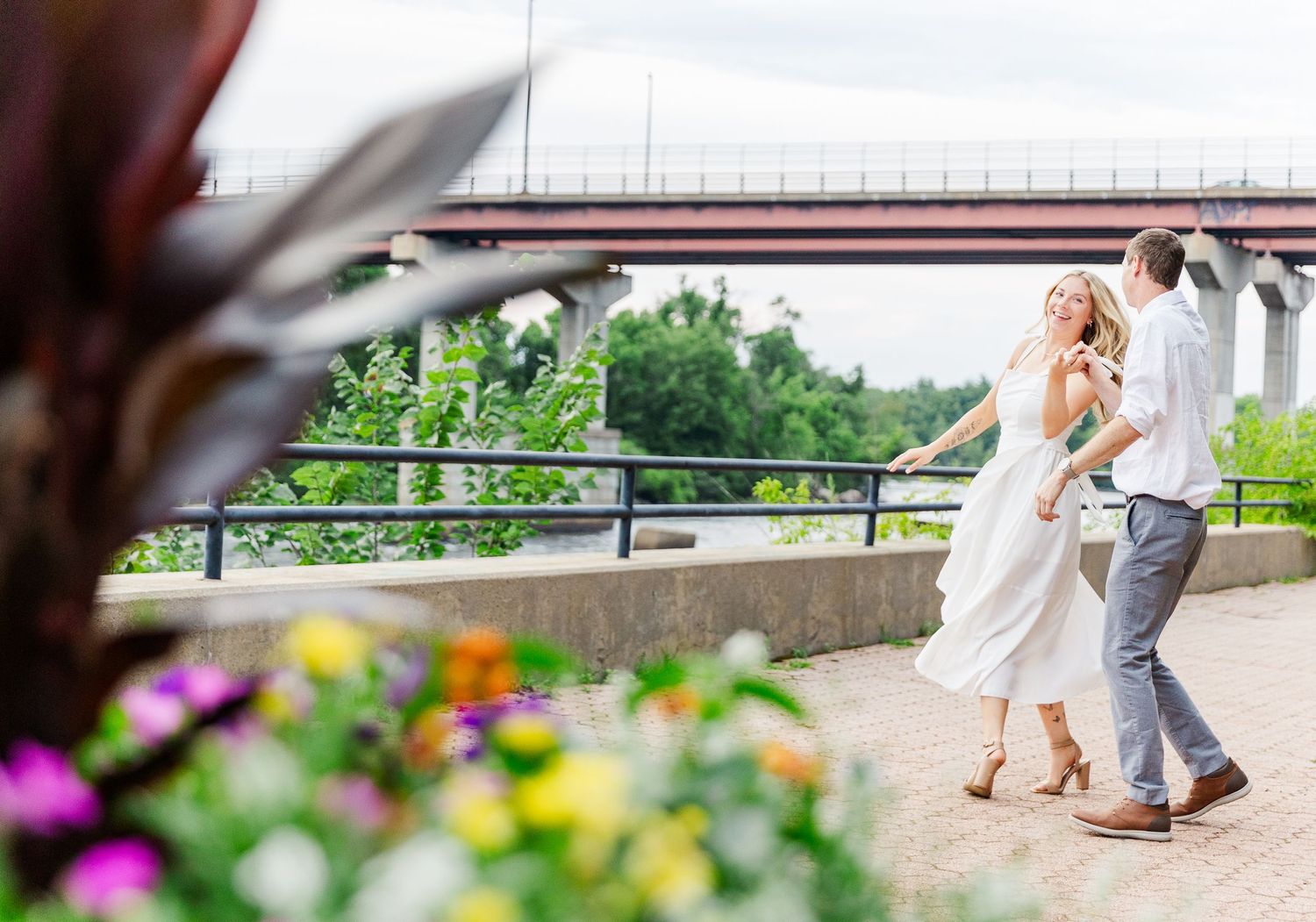 Dancing couple enjoying romantic moment near bridge with flowers in foreground.