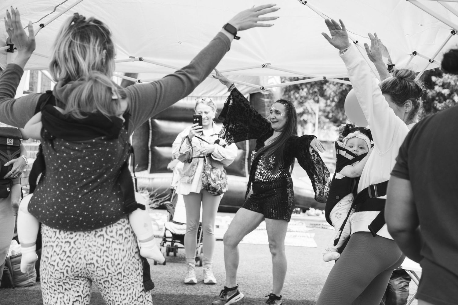People dance with raised arms at an energetic outdoor gathering.