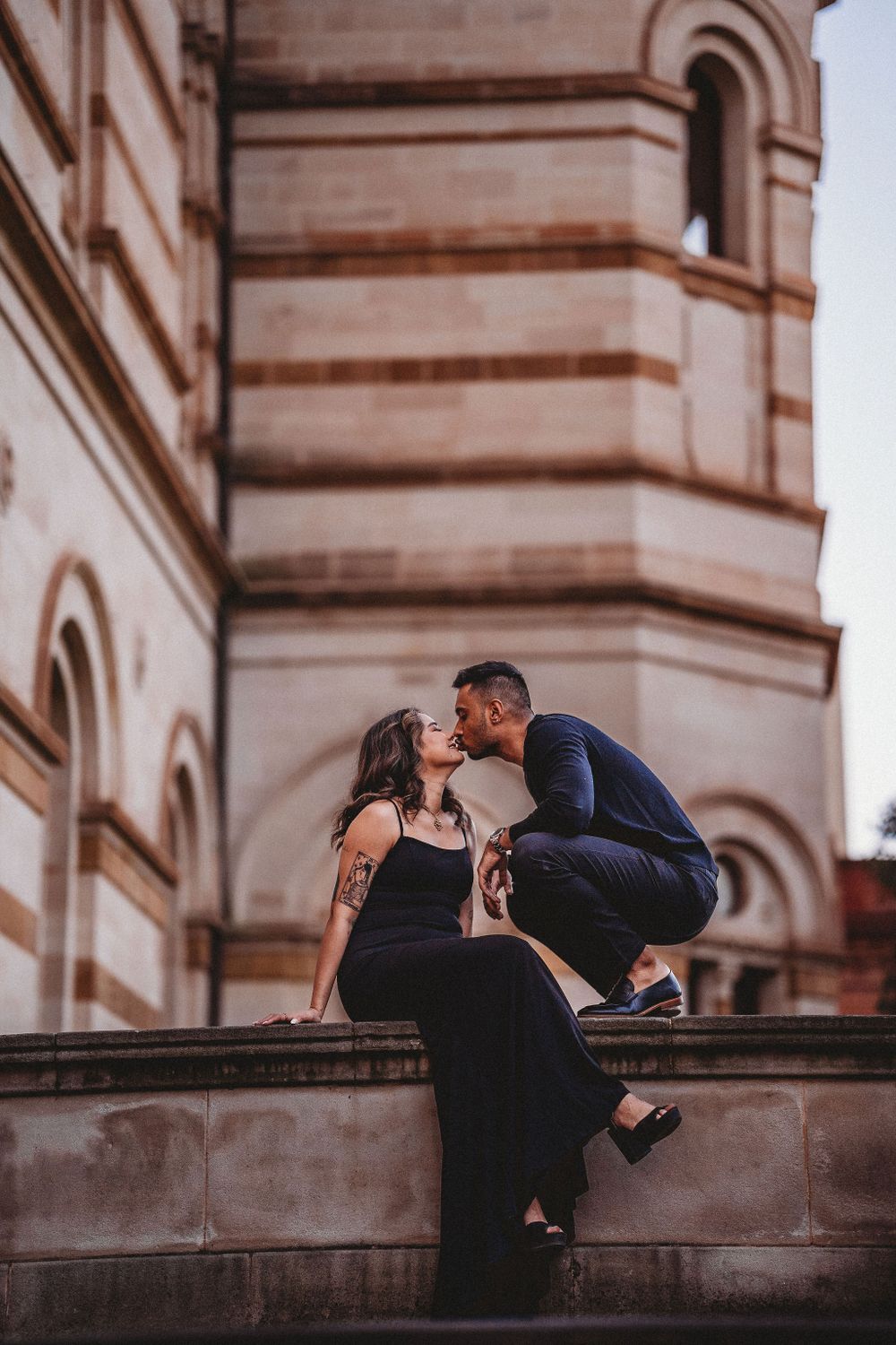 Romantic couple sharing an intimate moment on historic stone steps with ornate church architecture in the background.