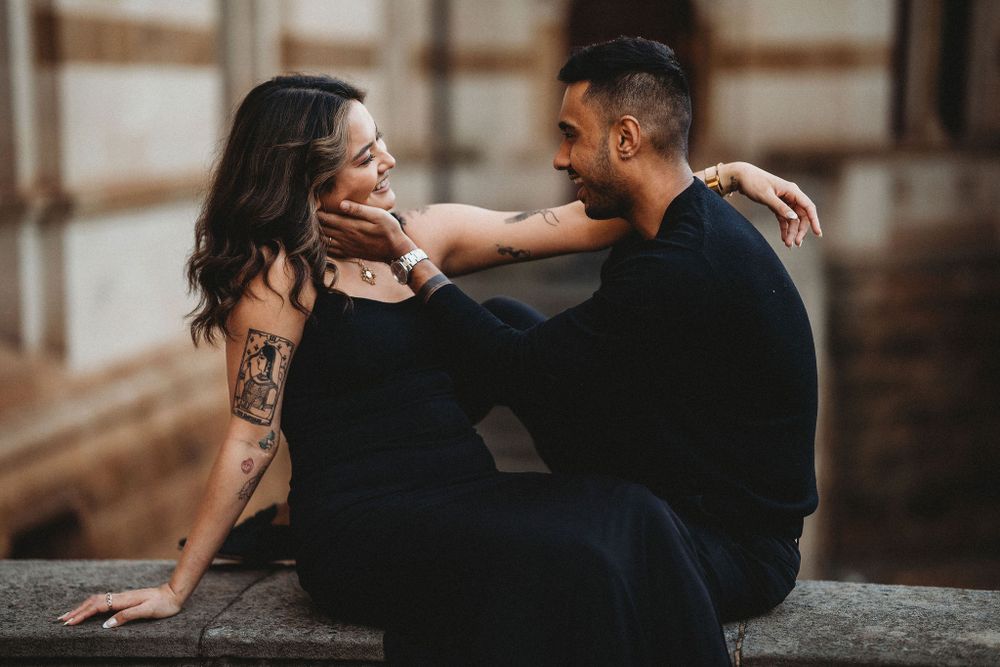 Couple in black attire sharing a tender embrace while sitting on stone steps during a sunset photoshoot.