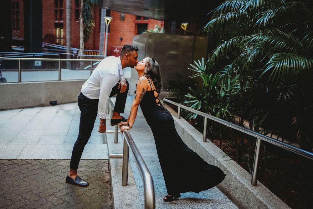 Couple in formal wear sharing a romantic kiss on an urban railing at dusk.