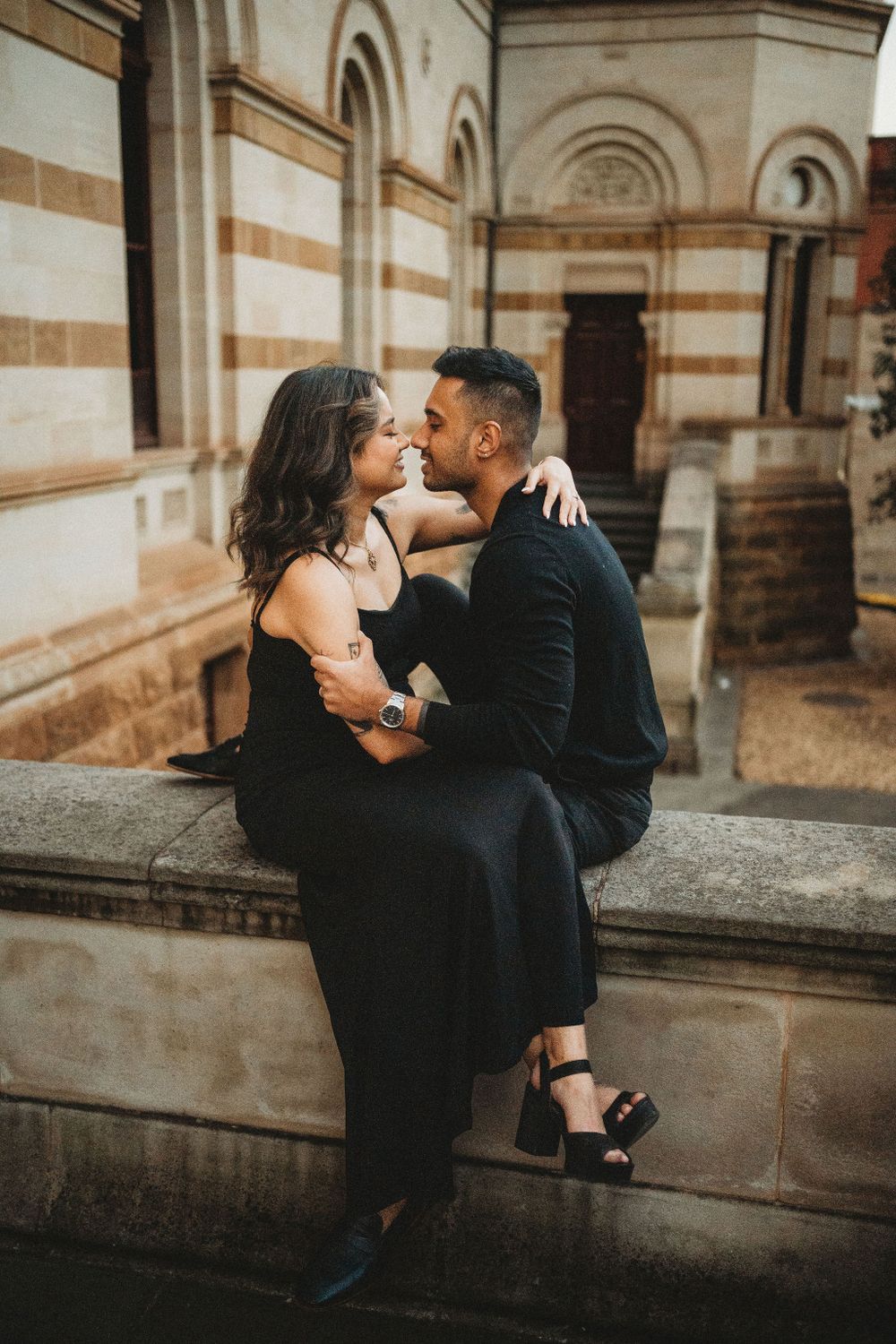A romantic moment captured against a beautiful stone building with arched windows.