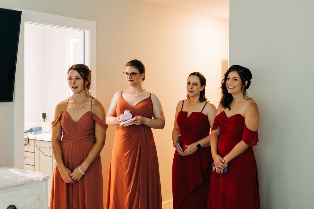 Bridesmaids in burgundy and rust-colored dresses stand together in an elegant room.