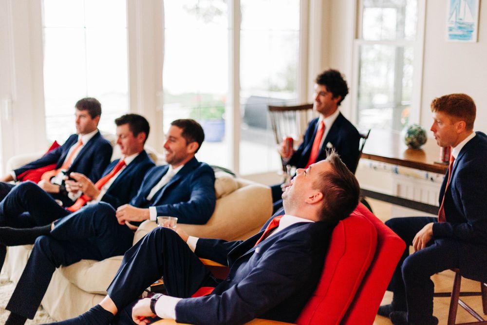 Group of men in dark suits relax on couches during formal event.