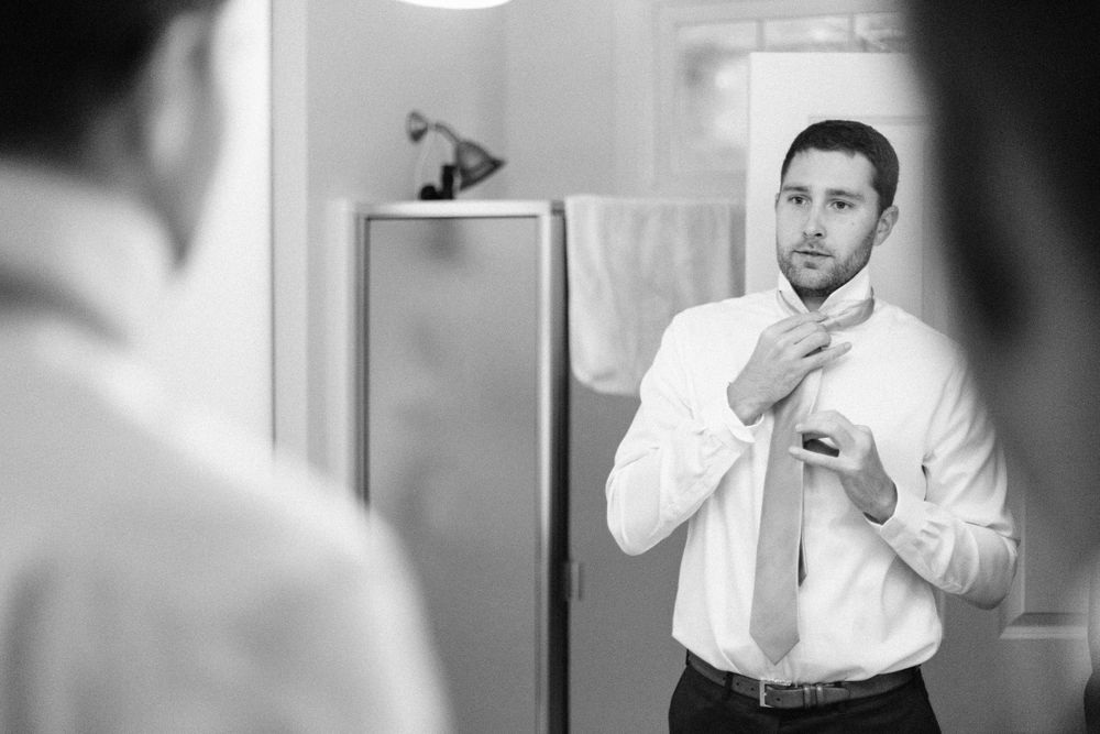 Person adjusting tie while looking in bathroom mirror wearing white dress shirt.